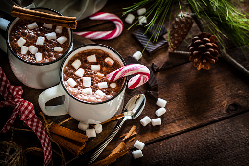 Two homemade hot chocolate mugs with marshmallows on rustic wooden Christmas table