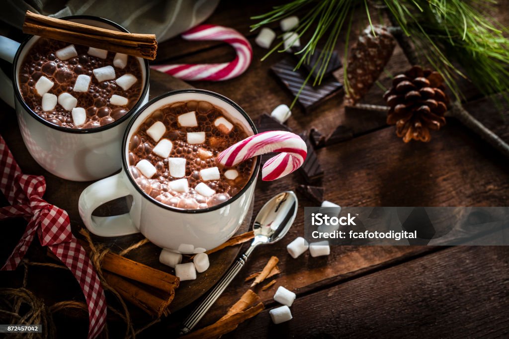 Two homemade hot chocolate mugs with marshmallows on rustic wooden Christmas table High angle view of two homemade hot chocolate mugs with marshmallows shot on rustic wooden Christmas table. A candy cane is inside one mug and another is placed directly on the table. Christmas decoration complete the composition. Low key DSRL studio photo taken with Canon EOS 5D Mk II and Canon EF 100mm f/2.8L Macro IS USM Christmas Stock Photo