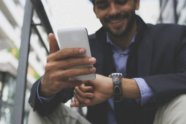 istock Businessman on city street checking time and using smart phone. Focus is on hands. 872475714