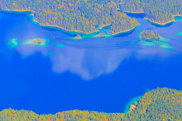 vista aerea della barca che attraversa il bellissimo e idilliaco lago turchese alpino eibsee con un lungo sentiero d'acqua, riflessione all'alba color oro in autunno, vista dall'alto zugspitze – paesaggio drammatico nelle alpi bavaresi – garmisch, bavi - zugspitze mountain lake autumn germany foto e immagini stock