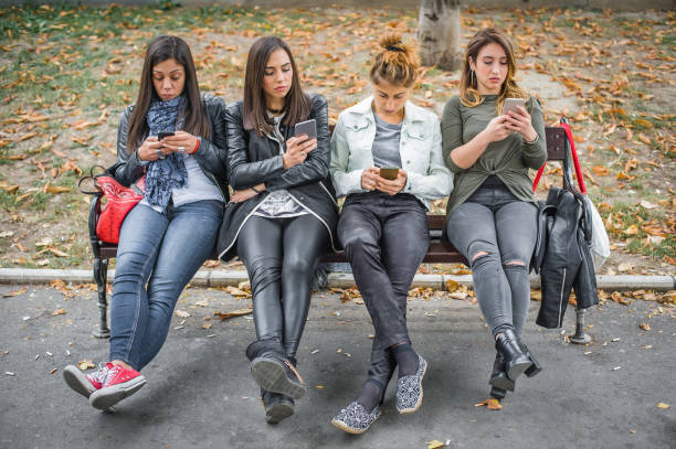 istock Group of girls using cellphones on park bench 872486882