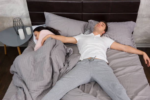Young male sleeping in free fall position with his girlfriend occupied the whole bed, wearing pajamas Young male sleeping in free fall position with his girlfriend occupied the whole bed, wearing pajamas, near bedside table with candles position stock pictures, royalty-free photos & images