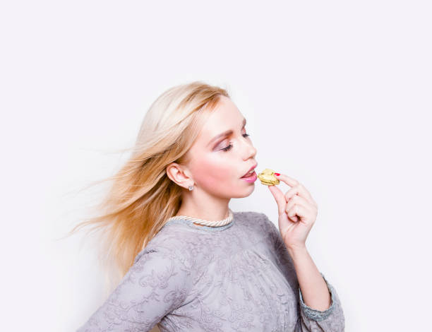 istock Beautiful glamorous young blond woman eating macaroon cookie 872491304