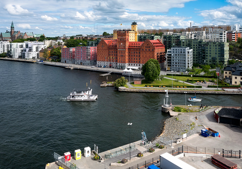 Two boats entering the Danvikskanalen navigation channel in Stockholm, capital of Sweden, on a sunny early summer day. The red building is the former Saltsjökvarn mill in Nacka, a suburb of Stockholm, and is now a hotel. The flat-bowed boat is the MS Molly, a charter boat. (Background people.)