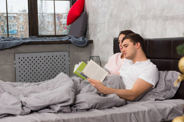 istock Young concentrated pair reading books while lying in the bed, outside the window snowing 872501824