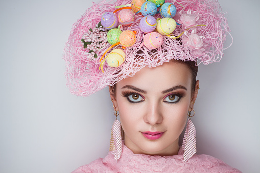 Bright pink hat, small eggs on woman head. Creative beauty professional makeup. Portrait of a beautiful lady who wore big accessory. conceptual idea banner. Greeting card Happy Easter, Christ is risen