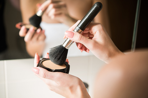 A close-up shot of a woman in a bathroom putting powder on a make-up brush.