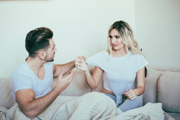 Boyfriend gripping girlfriend's T-shirt A young couple is seen on the sofa arguing while boyfriend is gripping girlfriend's T-shirt. clingy girlfriend stock pictures, royalty-free photos & images