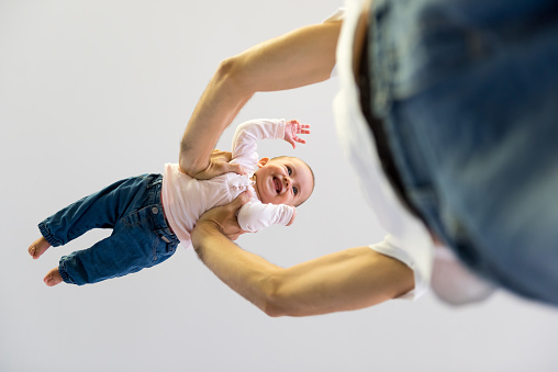 Low angle view of father lifting son against ceiling. Cheerful toddler enjoying with man. They are playing at home.