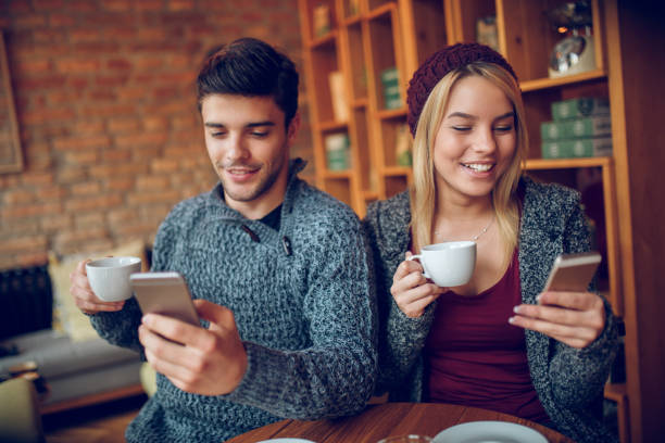 istock Young smiling couple with mobile phones in cafe 872542342
