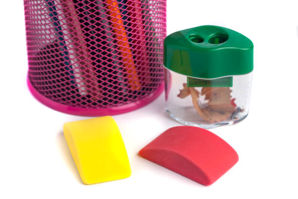 Photo of office equipment. Scattered randomly on a white background. Colored pencils, eraser, pencil sharpeners. Back to school. Pencils made of black wood. Pink, purple, blue, green.