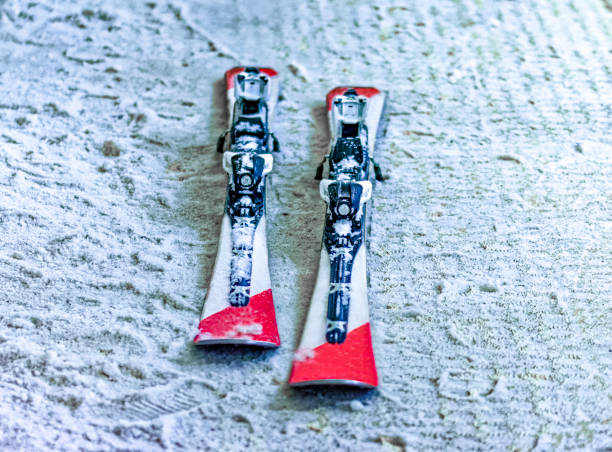 Single pair of skis sitting on artificial snow with no person using them having colors red white and black.