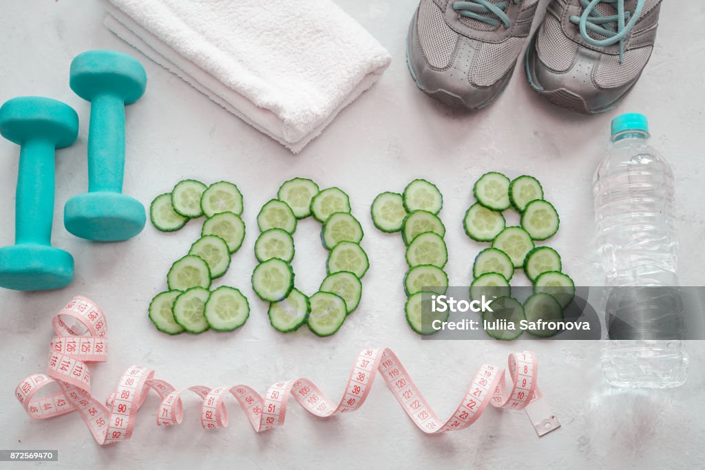 Sneakers, towel, water and dumbbells. Cucumber sliced symbol of the new year. Sneakers, towel, water and dumbbells. Cucumber sliced symbol of the new year. Diet 2018. 2018 Stock Photo