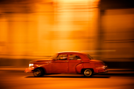 Motion blurred vintage American car goes down the street at night in Havana, Cuba