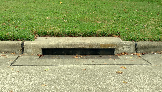 The entrance to a storm drain water runoff pipe tunnel on a suburban street, with a metal cover.