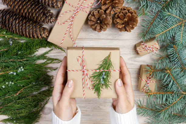 istock Christmas gift wrapping background. Female hands packaging christmas present wrapped in kraft paper top view. Winter holidays concept flat lay Woman holding Christmas gift box 872586260