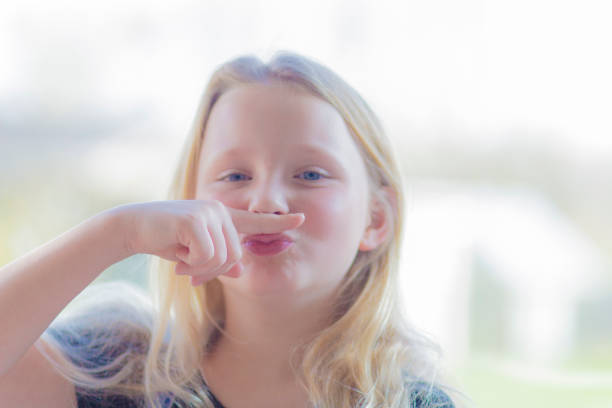 pre-teen rebel blonde making a finger moustache - costume mustache child disguise imagens e fotografias de stock