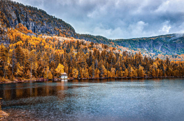 Lake house in autumn landscape by water during rainy cloudy day in Quebec, Canada with stormy clouds and dark weather Lake house in autumn landscape by water during rainy cloudy day in Quebec, Canada with stormy clouds and dark weather charlevoix photos stock pictures, royalty-free photos & images