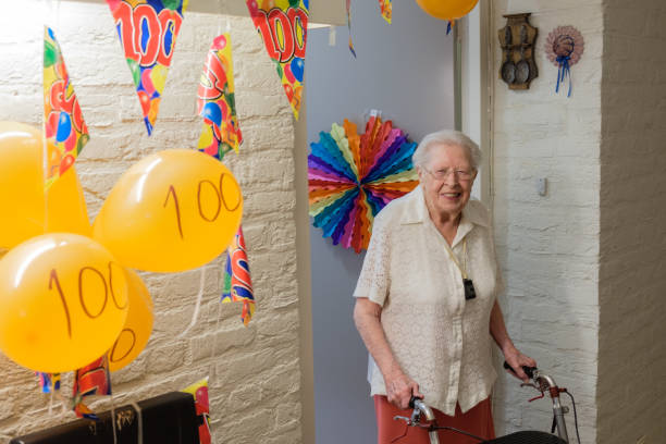 年配の女性は彼女の 100 th 誕生日を祝う彼女の飾られた部屋のドアの前に立つ - 100 satisfied ストックフォトと画像