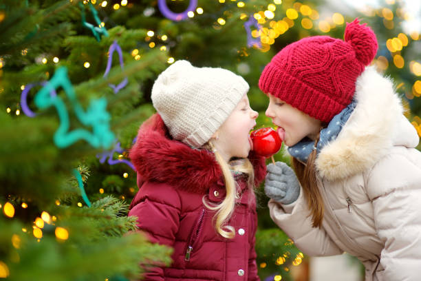 istock Two adorable little sisters eating red apples covered with sugar icing on traditional Christmas market 872618882