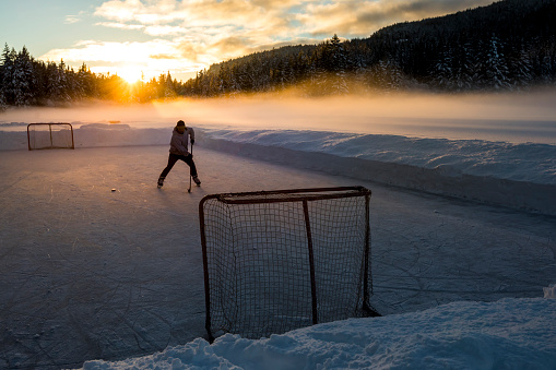 One adult skating on frozen lake during sunset, playing pond hockey.
