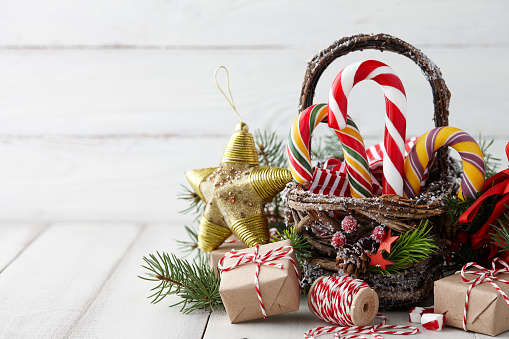 Christmas wicker basket with striped candy canes and wrapped gifts on white wooden table, festive decoration