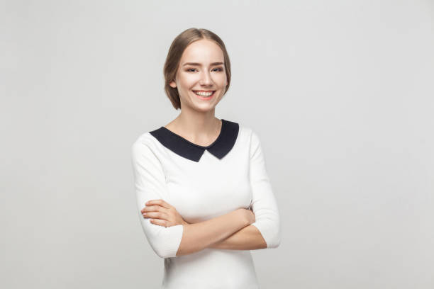 Businesswoman crossed hands, toothy smiling and looking at camera Businesswoman crossed hands, toothy smiling and looking at camera. Studio shot, gray background dressy girl stock pictures, royalty-free photos & images