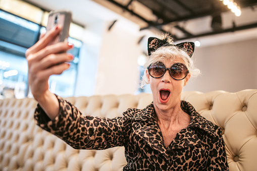 A fun and cheerful senior woman enjoys a day out on the town in the city of Portland, Oregon.  She wears fashionable clothing with a bit of flair and playfulness, enjoying a meal in a local food establishment.