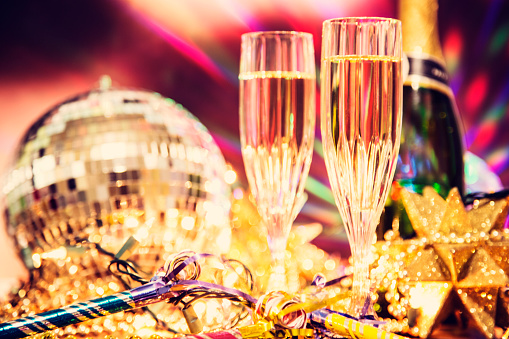 New Year's Eve celebration party with champagne, glasses, disco ball, decorations including beads, lights, blow horns and confetti.