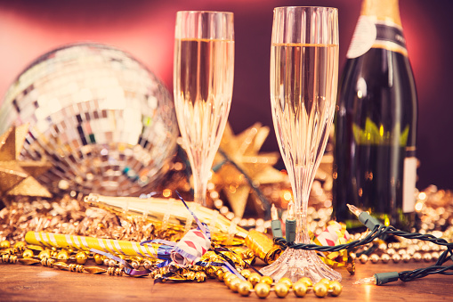 New Year's Eve celebration party with champagne, glasses, disco ball, decorations including beads, lights, blow horns and confetti.