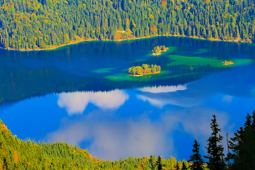Aerial view of Beautiful and idyllic Eibsee alpine turquoise lake with reflection at gold colored sunrise, view from above Zugspitze mountain peak – dramatic and majestic landscape in Bavarian alps, gold colored autumn  – Garmisch, Bavaria, Germany