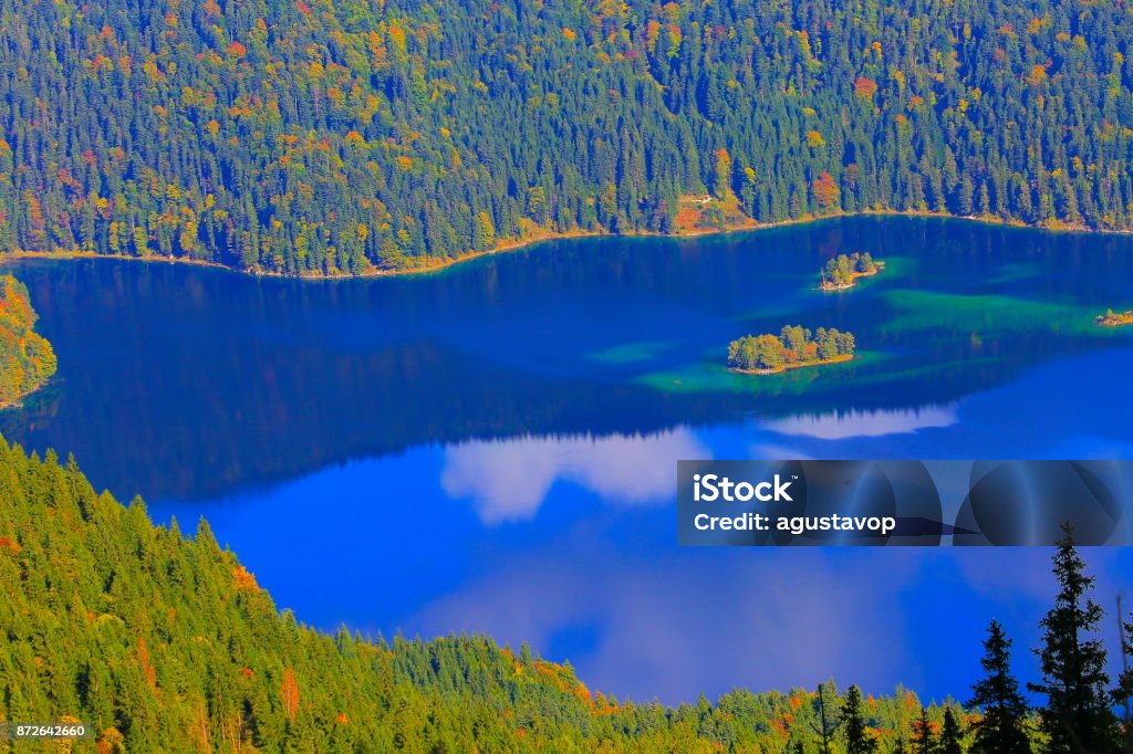 Aerial view of Beautiful and idyllic Eibsee alpine turquoise lake with reflection at gold colored sunrise, view from above Zugspitze mountain peak – dramatic and majestic landscape in Bavarian alps, gold colored autumn  – Garmisch, Bavaria, Germany Above Stock Photo