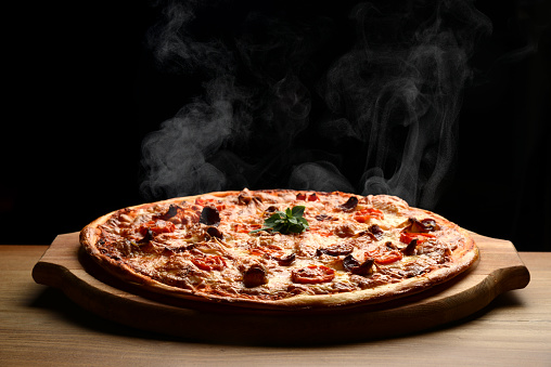 Hot big pepperoni pizza tasty pizza composition with melting cheese bacon tomatoes ham paprika steam smoke on black background