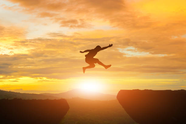 istock Men jump cliff sun light over silhouette 872677352