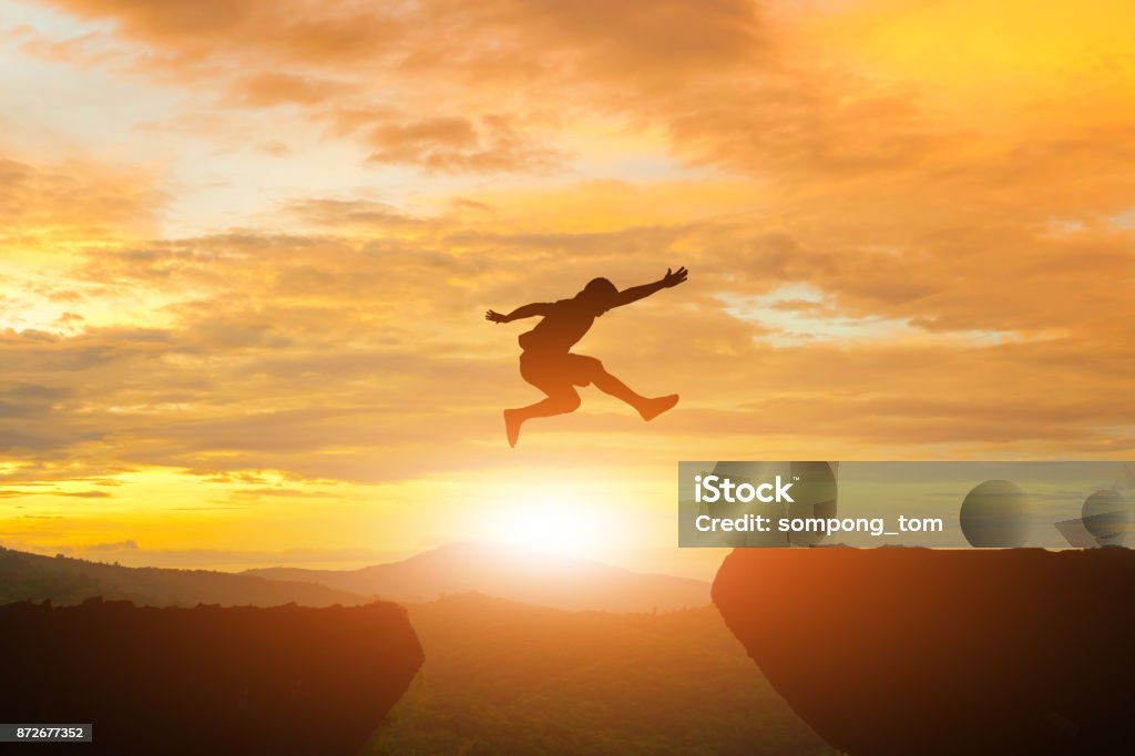 Men jump cliff sun light over silhouette Jumping Stock Photo