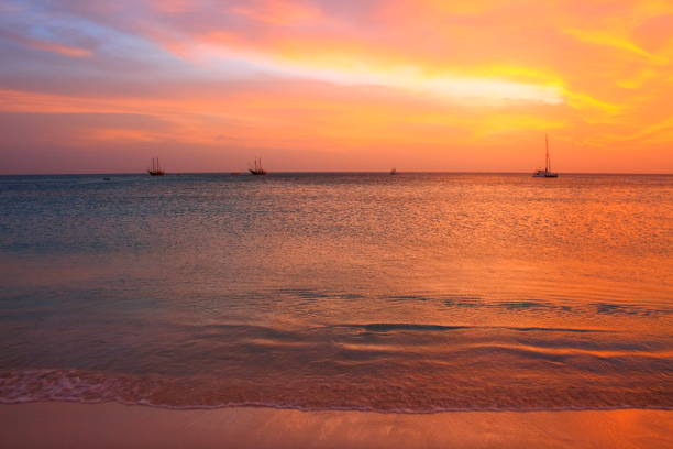 Sail boat sailing - Idyllic tropical Palm Beach at dramatic impressive gold colored sunset, sunny turquoise blue lagoon, summer paradise, Aruba – Dutch Antilles, Caribbean Blue sea