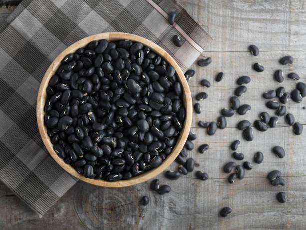Black beans in a wooden bowl, black beans in a wooden spoon on a wood background stock photo