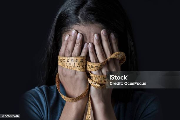 Close Up Hands Wrapped In Tailor Measure Tape Covering Face Of Young Depressed And Worried Girl Suffering Anorexia Or Bulimia Nutrition Disorder On Black Background Stock Photo - Download Image Now