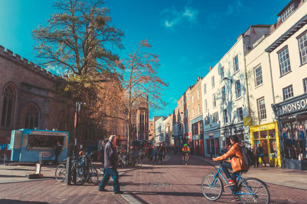 Street with college view and lots of Tourists and shoppers walking the street. Cambridge, England - October 23, 2017:  typical street scene in the old part of Cambridge at the university. The streets are still covered by cobble stones. People and shopper on the street high street shops stock pictures, royalty-free photos & images