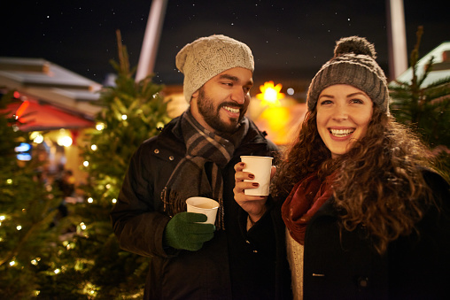 Shot of a happy young couple enjoying warm beverages at a Christmas night market