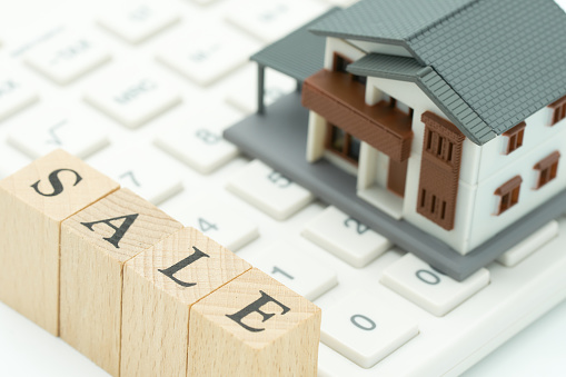 A model house model is placed on a calculator with wood word sale as background real estate concept with copy space.