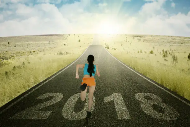 Back view of an Asian woman wearing sportswear while running toward sunlight with numbers 2018 on the road