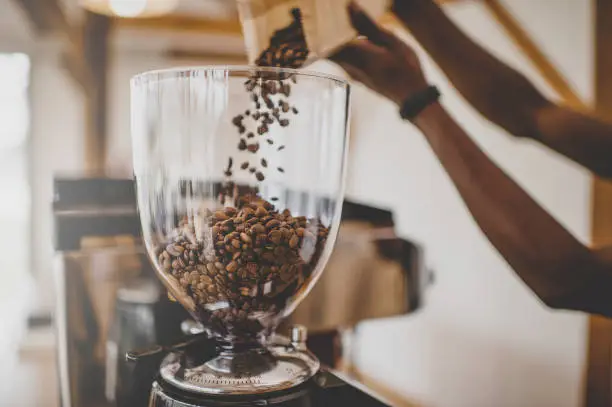 Black-African barista pouring roasted coffee beans into a glass grinder bowl from a packet of unmarked coffee Cape Town South Africa