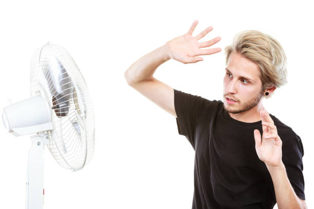 istock Young man fighting with wind from cooling fan 872742536