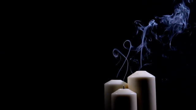 Three extinguished candles with smoke on a black background