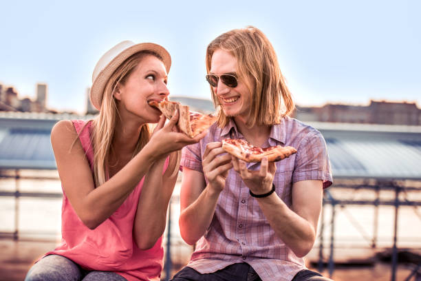 istock Young couple sitting outdoors and eating pizza. 872749922