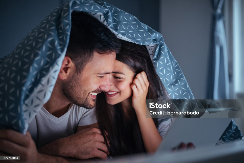 Late night movie date Young couple lying in bed at night , holding a tablet Movie Stock Photo