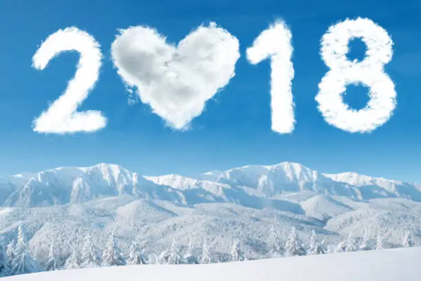 Beautiful snowy mountain with clouds shaped number 2018 and heart in the blue sky