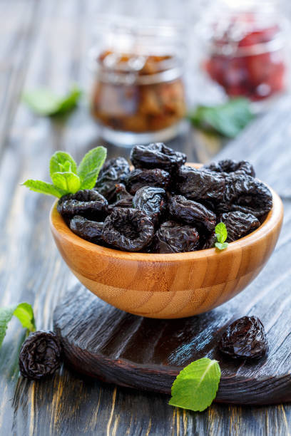 istock Dried black plums in a wooden bowl. 872762270