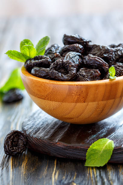 istock Wooden bowl with dried black plums. 872772622